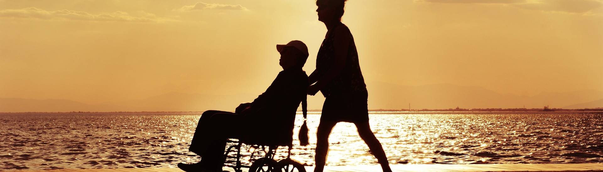 Personne en poussant une autre qui est en fauteuil roulant sur une plage ensoleillée