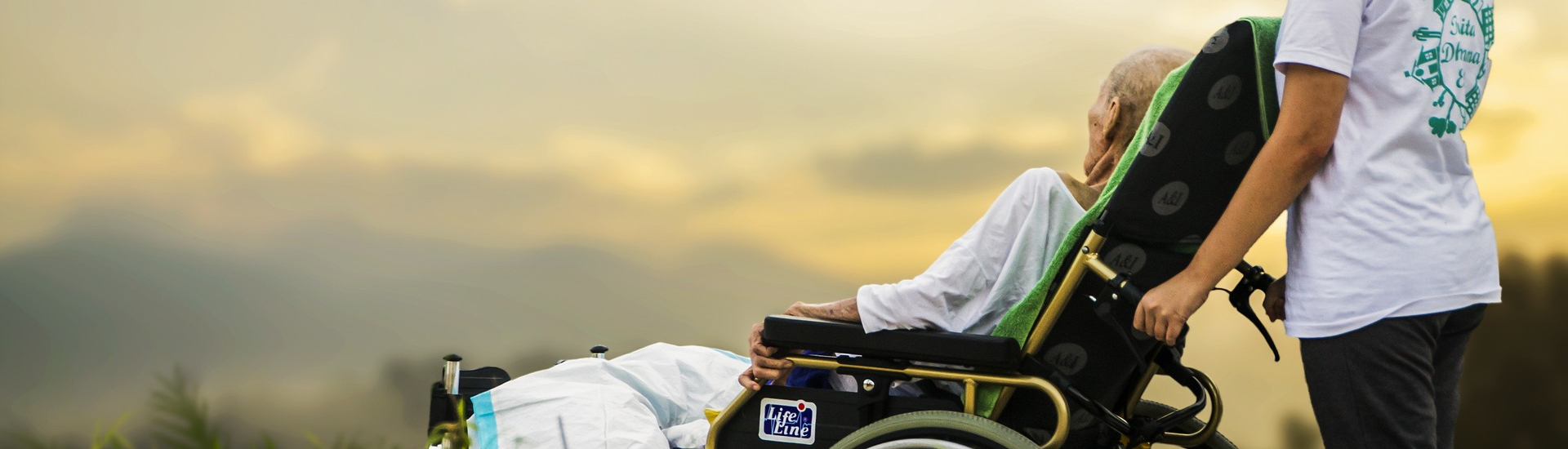 Personne handicapée âgée dans son fauteuil face au ciel nuageux et soleil couchant